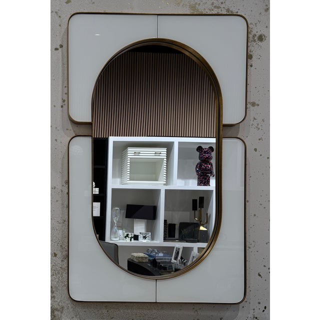 The clean and sophisticated Embrace Mirror has a white glass frame encased in an antique gold-leaf metal frame. It may be...