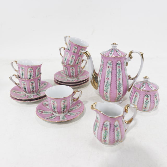 A stunning vintage porcelain tea set featuring a delicate pink floral design, vertical stripe patterns, and gold trim....