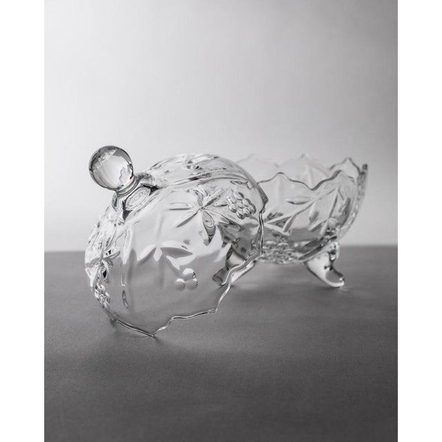 This vintage glass bonboniere from the 1980s is a graceful footed lidded bowl crafted in beautifully textured clear glass....