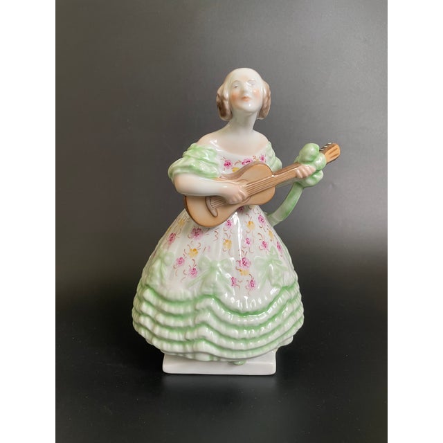 A exquisite Herend "Deryne" porcelain figurine features a charming girl in a mint green dress adorned with small flowers,...