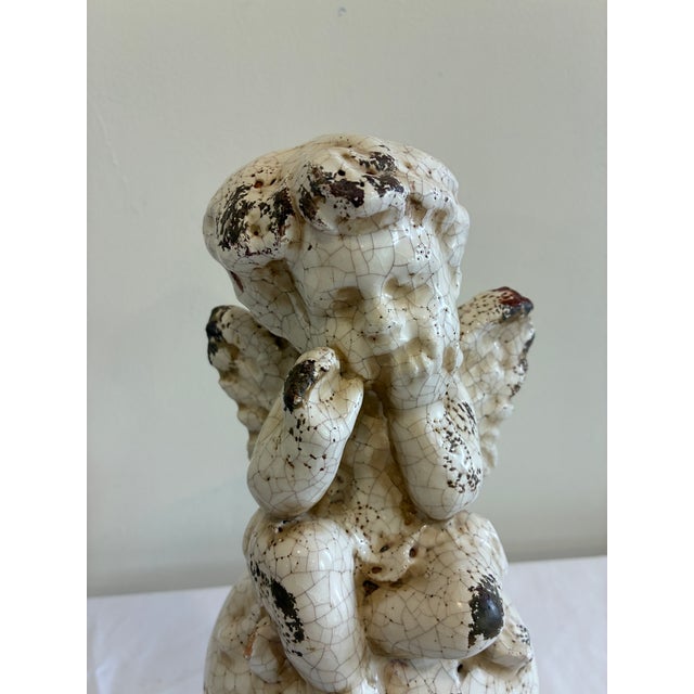 A charming vintage ceramic cherub statue featuring a heavily crackled cream glaze and antiqued finish. The seated angel is...