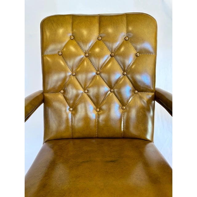 Mid-century armchair featuring a warm camel-toned vinyl upholstery with deep diamond tufting and wood frame detailing. The...