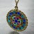 An 18 karat (18K) yellow gold charm pendant designed as a round medal with a rope-twist edge depicting a stained glass...