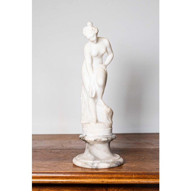 A French Neoclassical style marble sculpture from the 19th century depicting a nymph after the bath on a gray and white...