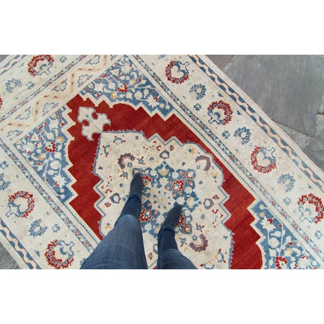 A striking, finely hand-knotted Oushak rug with a floral themed medallion on a vibrant sangria color background. With an...