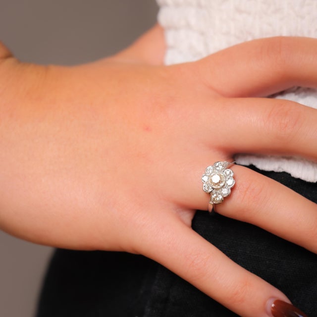 This Mid Century platinum flower cluster ring features a luminous 0.99-carat old mine-cut diamond surrounded by shimmering...