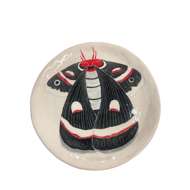 This striking, artisanal studio ceramic plate features a bold, graphic illustration of a moth (resembling a Cecropia or...
