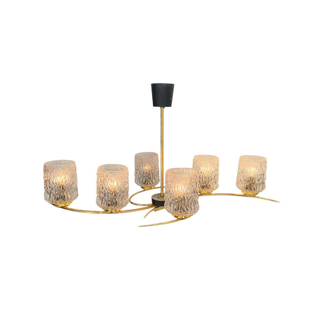 A particularly elegant 6-light brass chandelier with clear textured glass shades. The chandelier features a striking and...