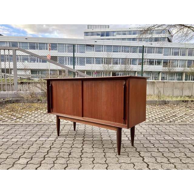 Elegant Mid-Century teak sideboard featuring sliding doors and beautiful detailing on both the legs and door handles. The...