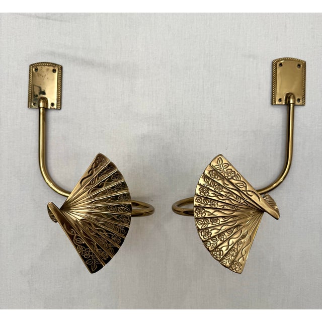 This pair of Hollywood Regency style drapery tie backs feature a singular curved arm with a three dimensional , intricate...