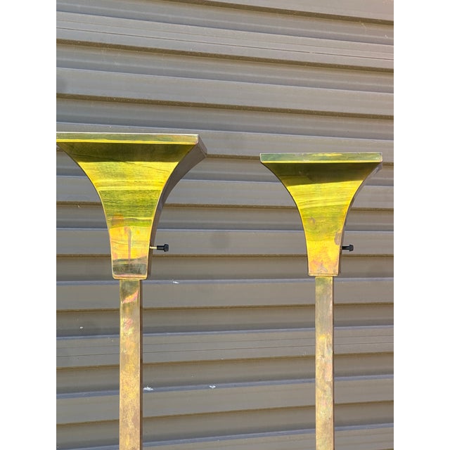 Pair of tall brass torchieres with square stepped bases and a clean, architectural silhouette. Each lamp features a rich...