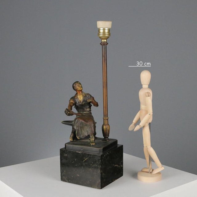 Bronze sculpture on a black marble base transformed into a table lamp. A statue of a blacksmith seated at an anvil rests...