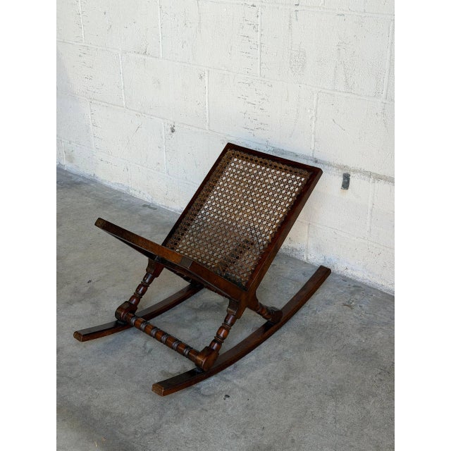 A distinctive Danish rocking magazine rack featuring a dark wood frame, turned supports, curved rockers, and woven cane...