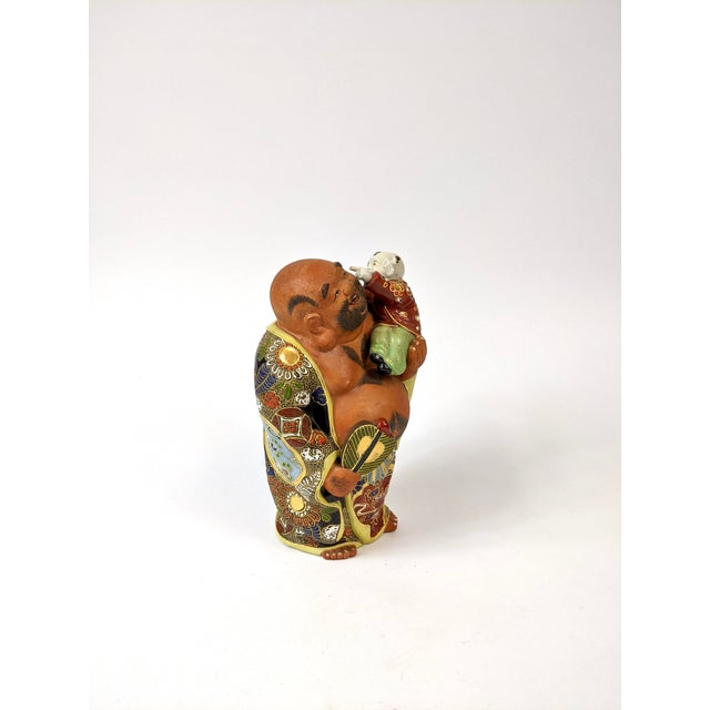 A Happy Buddha holding a small baby! This is Japanese Kutani-ware which is marked by vivid dark colors which traditionally...