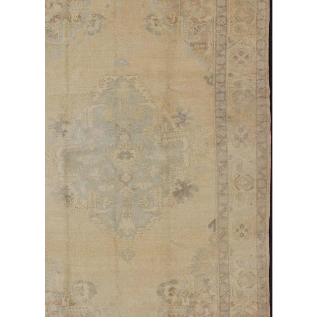 Oushak Vintage Turkish rug with faded central medallion in cream, soft yellow, accent light blue and muted tones, rug...