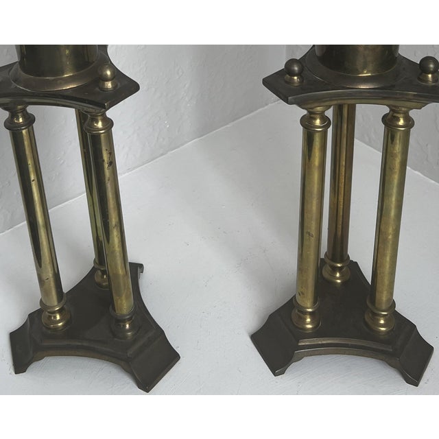A striking pair of vintage brass hurricane candle holders featuring tall clear glass shades and sculptural architectural...