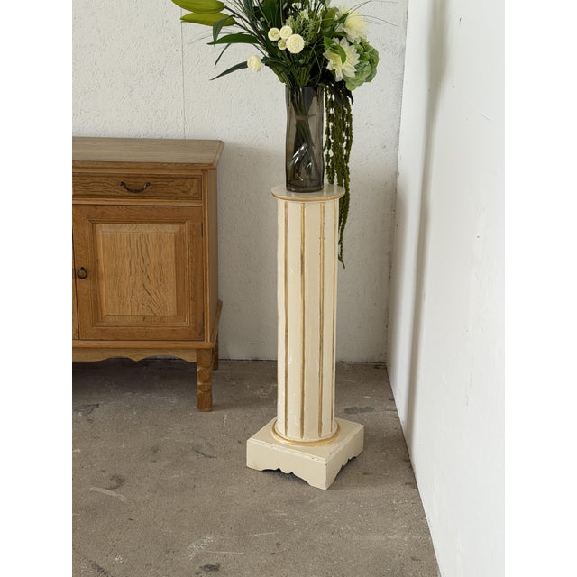 This pedestal columns is painted in a soft cream tone with gilt detailing, produced in the Gustavian style during the 20th...