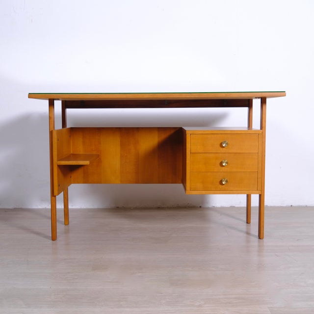 This vintage wooden desk in mid-century Italian style from the 1950s features three side drawers and a glass top. The...