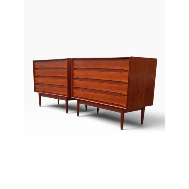 A matched pair of Danish modern four-drawer dressers in richly figured teak, by Arne Vodder. Full-width sculpted pulls are...