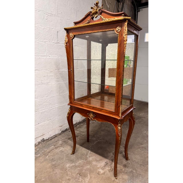 An elegant Louis XV–style vitrine cabinet crafted in beautifully figured walnut veneer wood with cast brass ormolu...