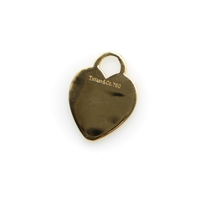 This is a blank Tiffany & Co. 18k gold charm, an iconic piece reminiscent of a luggage tag shaped like a heart. This...