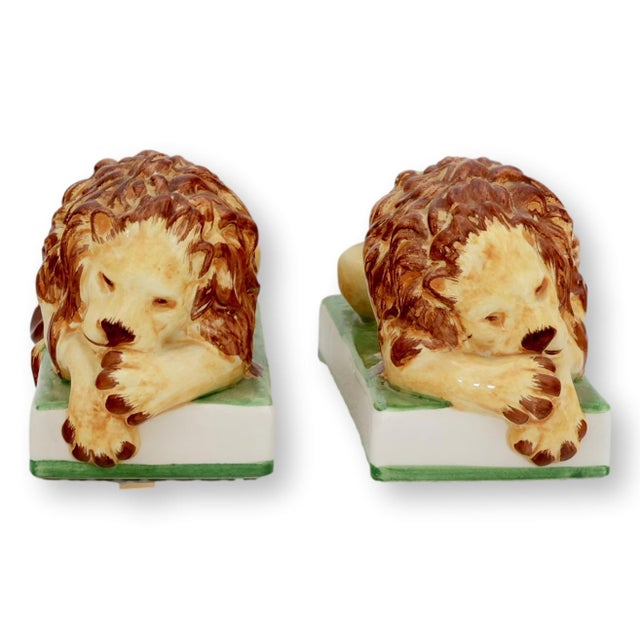 Mid 20th century Italian faience lions modeled in reclining form with expressive hand painted features and warm cream,...