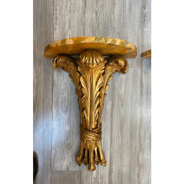 A pair of chic high style Hollywood Regency gilt and faux painted marble demi lune wall hanging tables. The acanthus leaf...