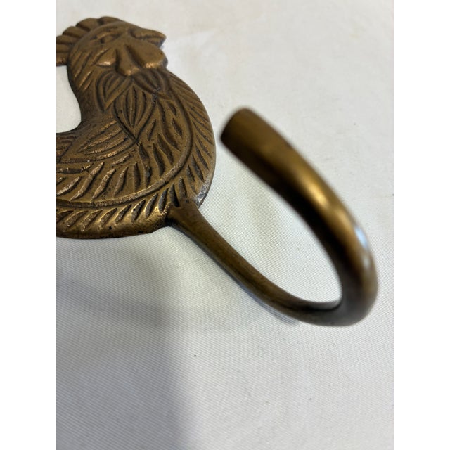 A charming vintage brass rooster with detailed feather etching, a proud ridged comb, and a single hook below. A keyhole...