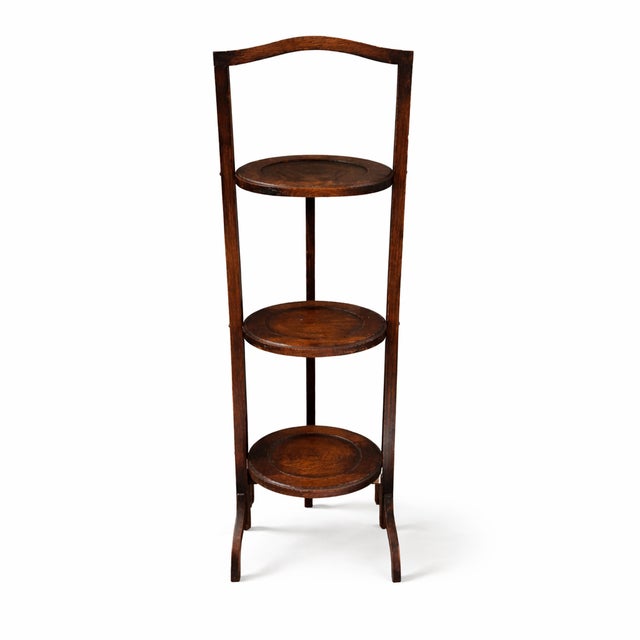 A tall three-tier serving stand with a refined vertical structure and rich dark wood tone, reflecting early 20th-century...