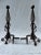 A matching pair of antique iron andirons with twisted open finials and ring handles. The pair retains its original dark...