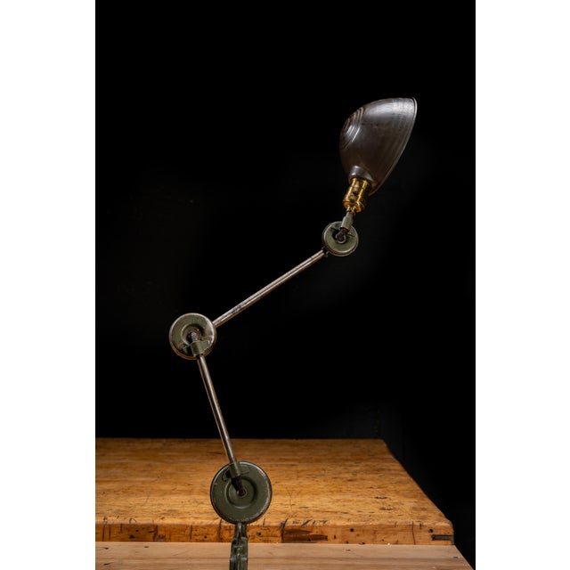 Industrial articulating task lamp featuring a heavy cast iron clamp base, dual articulating steel arms, and a spun...