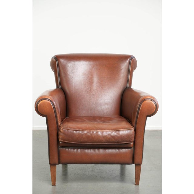 This timeless armchair, made of sheepskin and featuring an English-style design, has a warm cognac color and a beautiful...