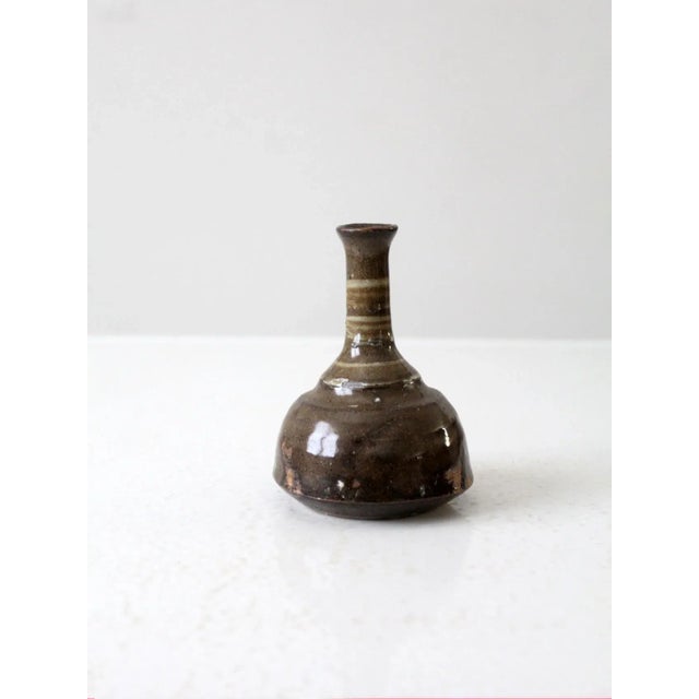 This is a vintage studio pottery vase. The handmade vase has a long bottleneck with a warm olive brown glaze.