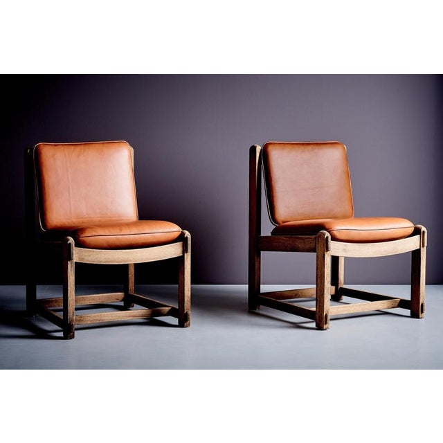 A sculptural lounge chair crafted from solid oak, featuring a sturdy square frame with visible pegged joinery. The curved...