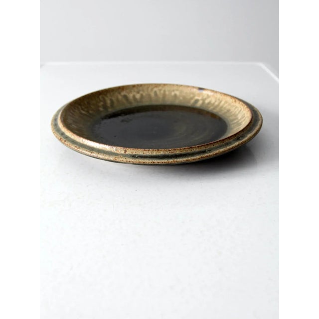 Vintage studio pottery plate, hand-crafted with a large, sculptural form. This ceramic plate features a richly layered...