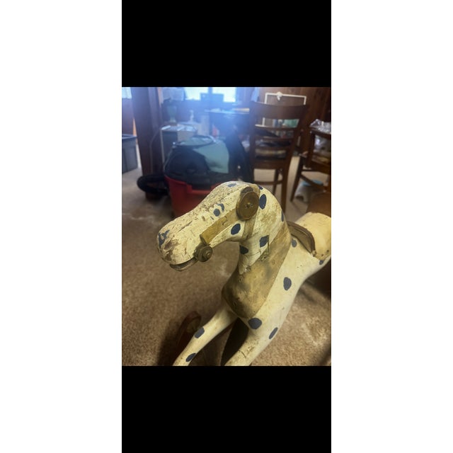 A charming early 20th-century wooden rocking horse featuring its original hand-painted surface with whimsical blue polka-...
