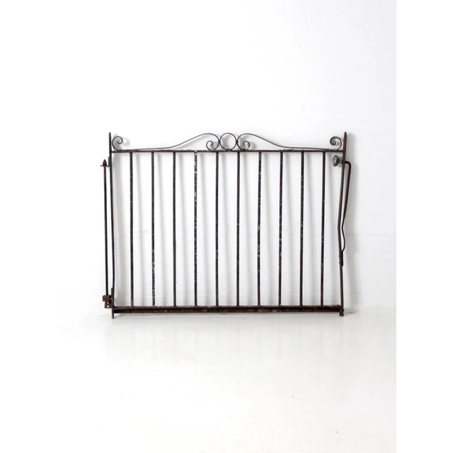 This antique wrought iron gate features classic scrollwork and a richly weathered patina with patches of lichen that speak...