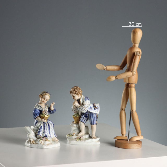 A pair of porcelain children with a basket of polychrome flowers, hand-decorated in blue and white. Manufacturer's mark...