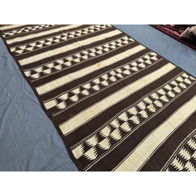 Welcome! This beautiful vintage flat weave kilim rug features a striking geometric design in earthy brown and ivory tones....