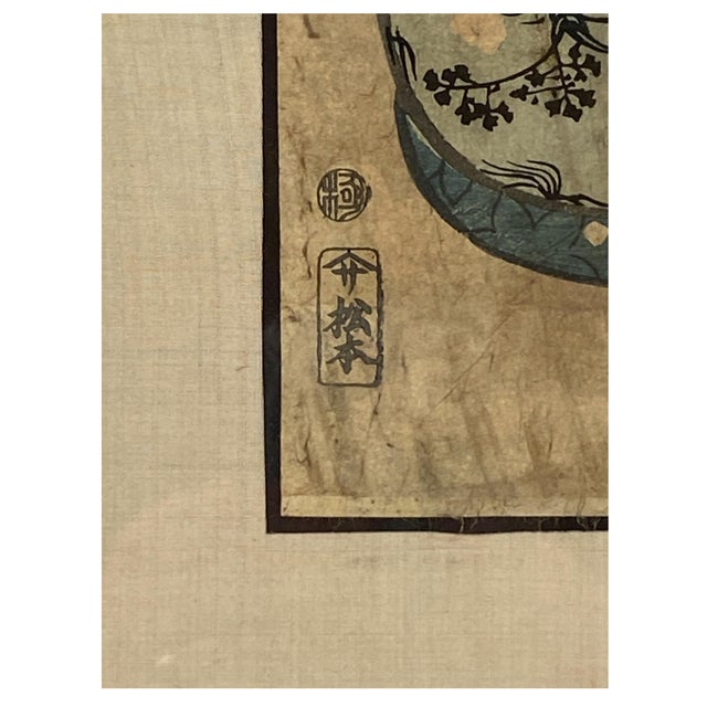A framed Edo period Japanese vertical color woodblock print of a woman in an elaborate topknot with hairpins stoops to...