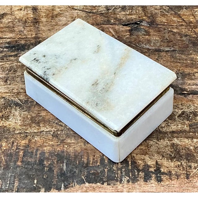 This trinket box is defined by the quiet elegance of natural stone, its rectangular lid and base carved from a soft,...