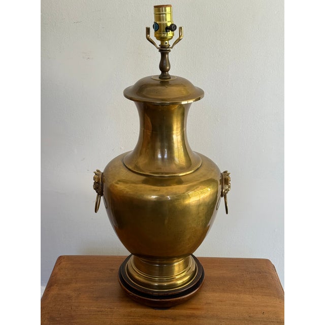 A midcentury Hollywood Regency polished brass urn table lamp with foo-dog ring handles on a dark wood plinth, classic...
