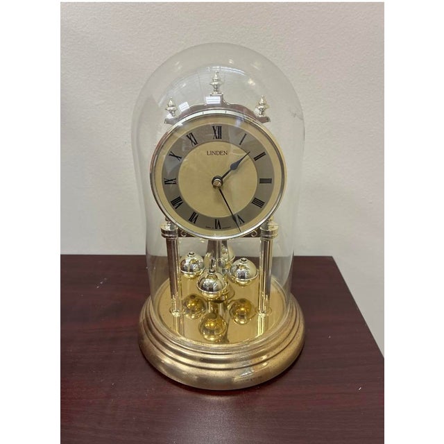 A 9-inch-tall gold quartz anniversary dome clock by Linden with roman numerals and a rotating pendulum mechanism. It's...