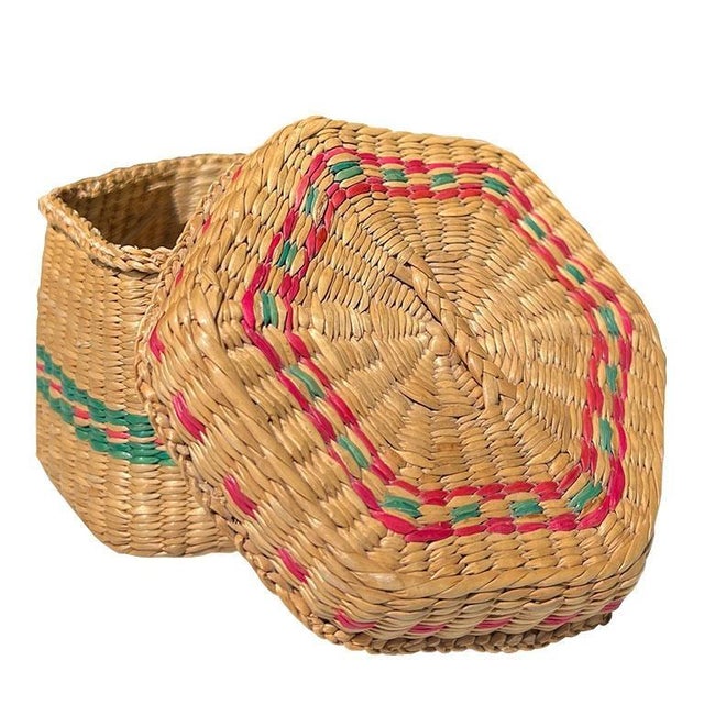 A six-sided woven sweet grass decorative basket in brown, with bright green and pink decorative design. This basket is...