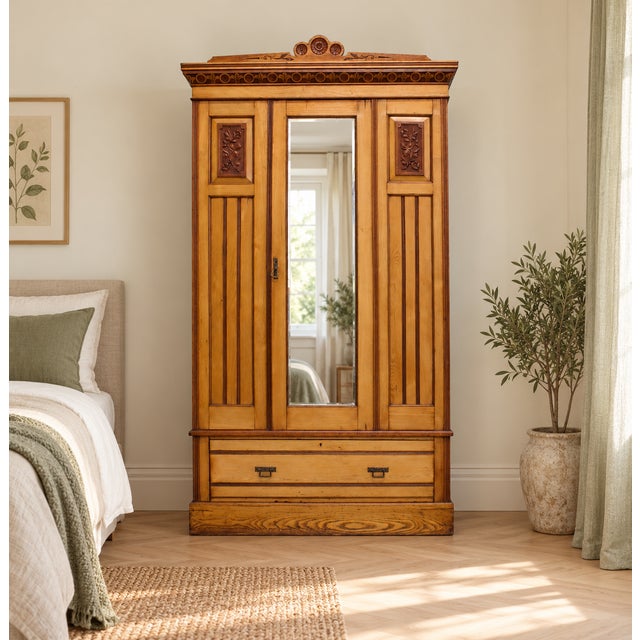An Edwardian ash wardrobe with Arts and Crafts influence, featuring a decorative carved crest, floral carved panels, a...