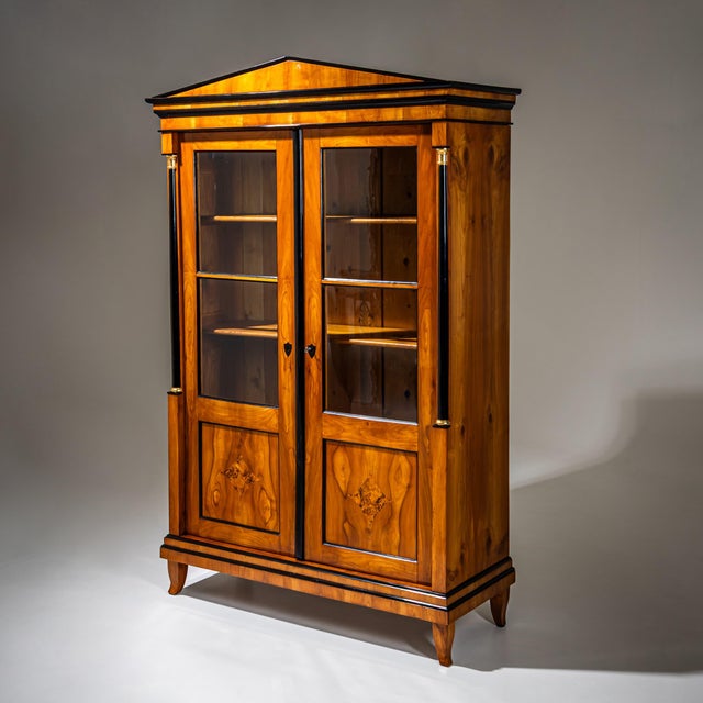 Biedermeier bookcase veneered in cherrywood with ebonized columns and moldings. The cabinet stands on slightly curved...