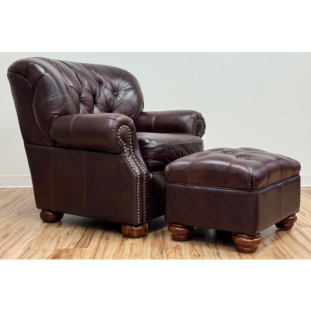 Classic vintage tufted wingback chair and ottoman upholstered in a warm brown leather. Features deep button tufting on the...