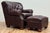 Classic vintage tufted wingback chair and ottoman upholstered in a warm brown leather. Features deep button tufting on the...