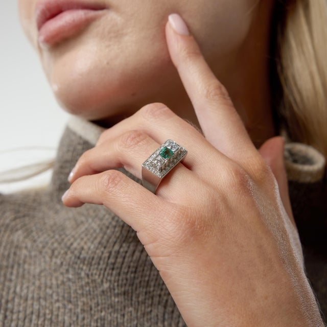 A bold statement of 1940s design, this Retro tank ring showcases a vivid emerald cut emerald at its center, framed by an...