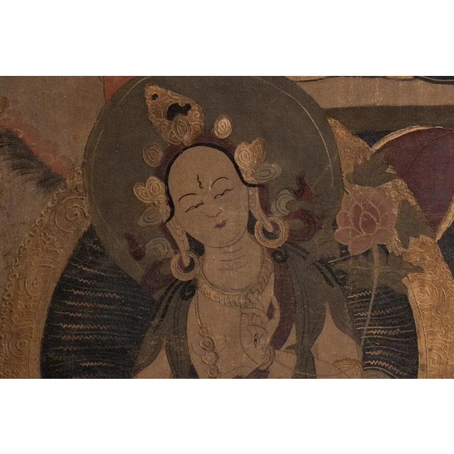 Tibetan Thangka painted on canvas representing a Buddha and characters, framed by a thin black wooden stick. Indian work...